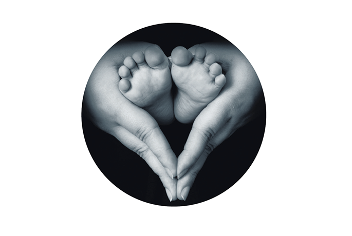 A black and white close up of a newborns feet being held by two hands